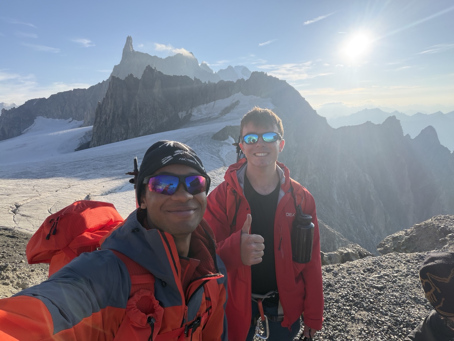 Two climbers smiling in clear weather with alpine peaks behind them